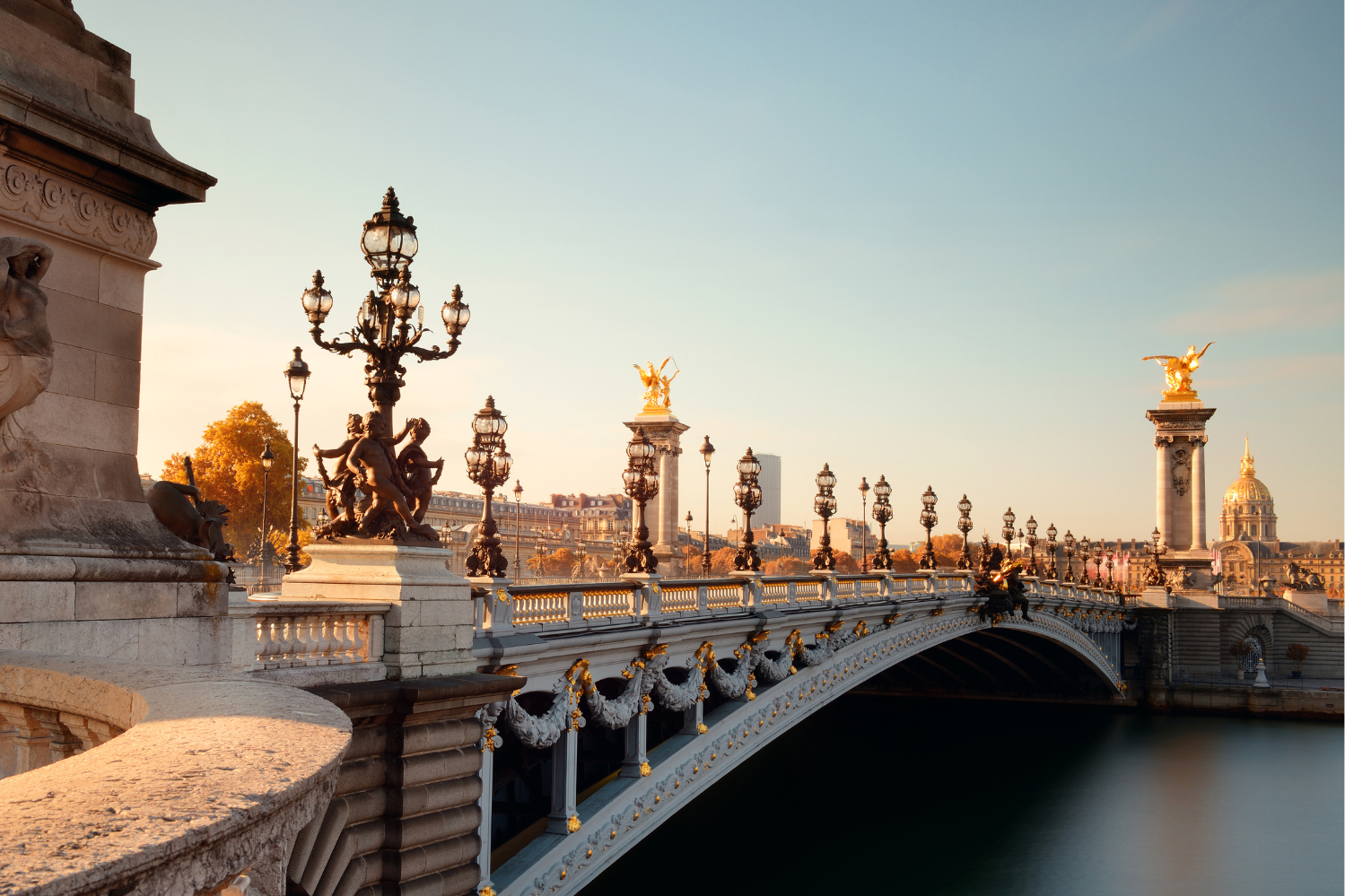 Vue pittoresque du Pont Alexandre III à Paris au coucher du soleil, mettant en valeur ses réverbères ornés, ses statues dorées et ses détails architecturaux raffinés baignés d'une lumière dorée.