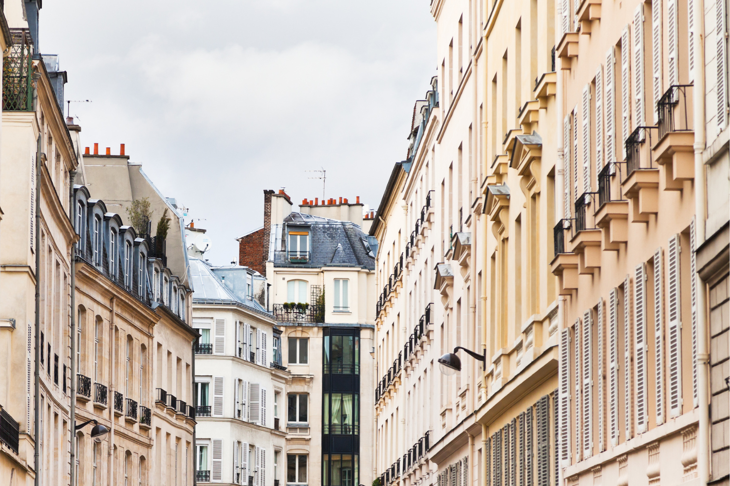 Vue pittoresque d'une rue parisienne bordée de bâtiments traditionnels avec des façades élégantes, des balcons en fer forgé et des fenêtres typiques de l'architecture parisienne.